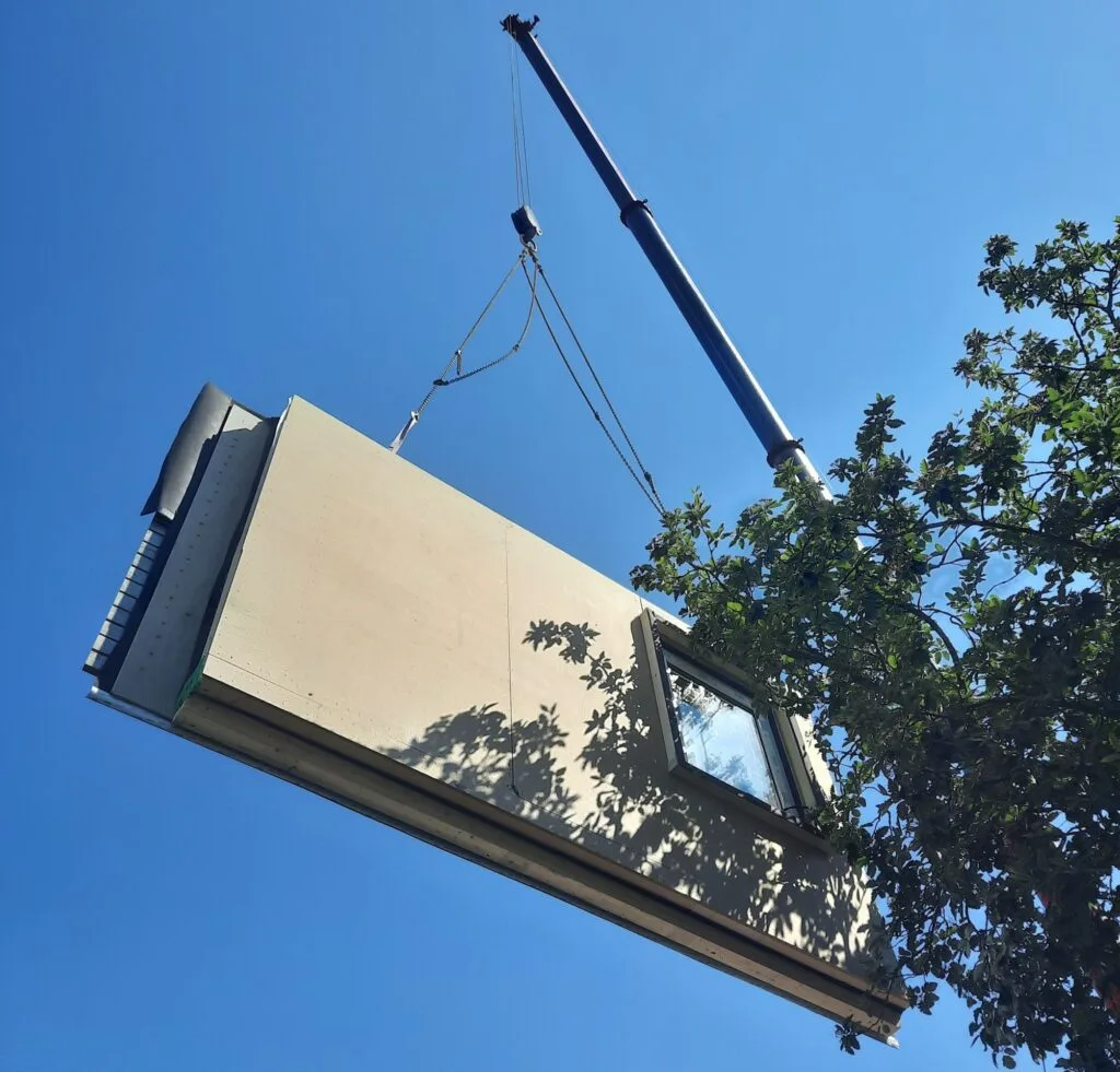 Vorgefertigtes Wandelement wird auf der Baustelle per Kran an ihren Platz gehoben.