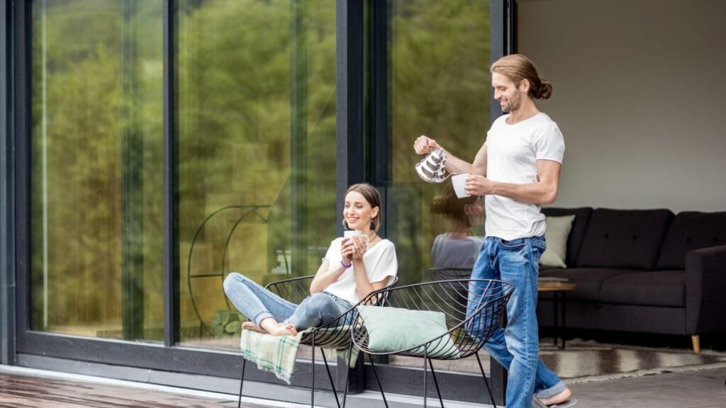 Young couple sitting with cups on the terrace of the modern house enjoying beautiful view outdoors. www.elements-envato.com