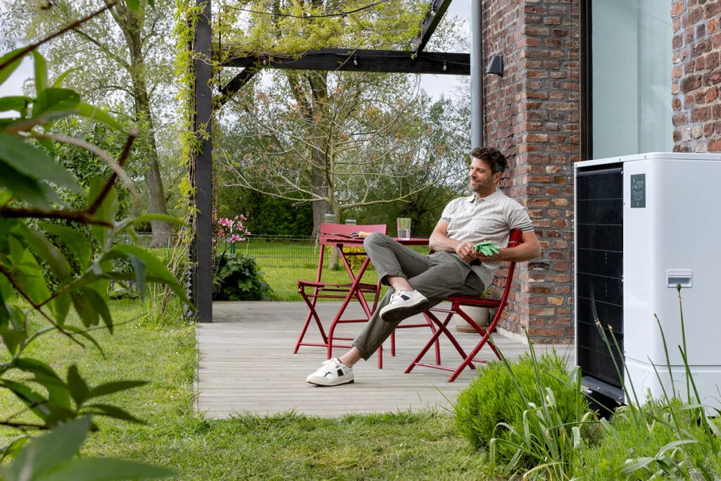 Mann sitzt im Garten neben Wärmepumpe
