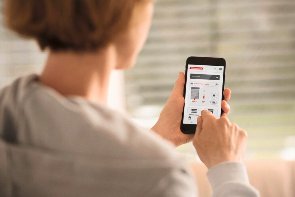 Frau bedient eine App zur Sonnenschutz Steuerung auf ihrem Smartphone.