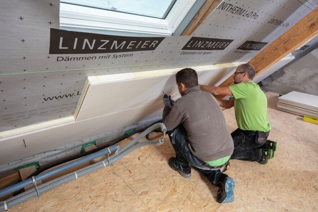 Zwei Handwerker bringen eine Gipskartonplatte am Dachinneren an