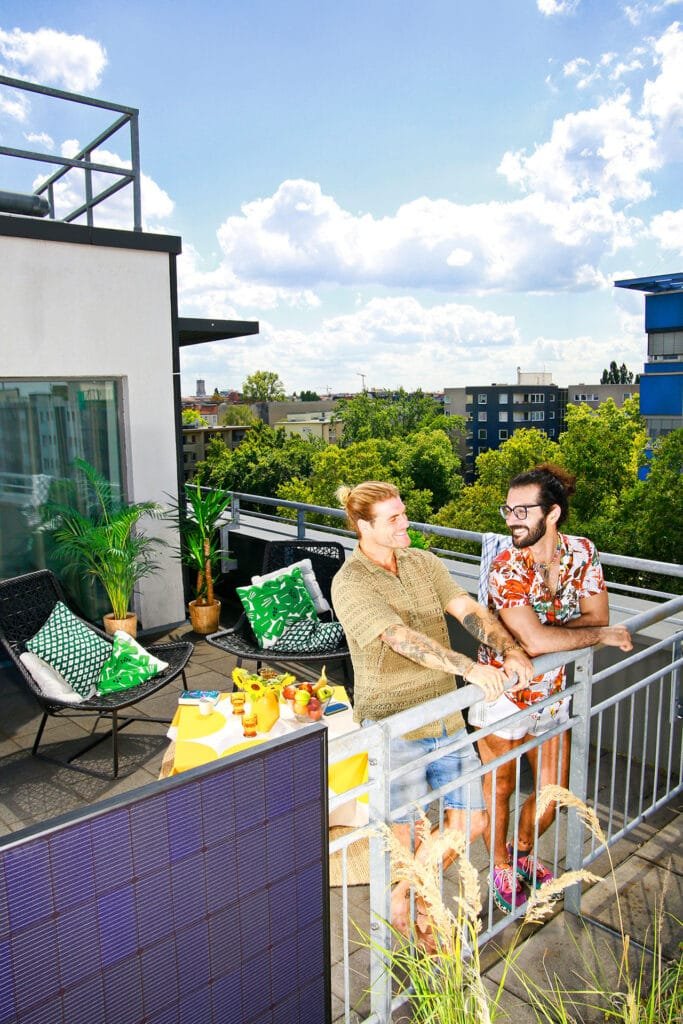 Das Foto zeigt zwei Männer, die an einem Balkongeländer mit Steckersolaranlage lehnen.