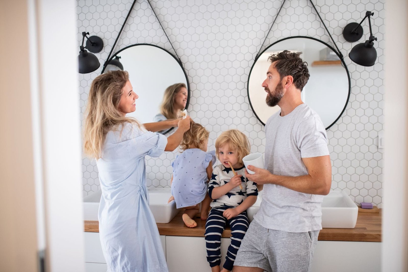Eine junge, glückliche Familie im Bad vor zwei Wachbecken. Die Eltern stehen und die Kinder sitzen zwischen ihnen auf dem Waschtisch.