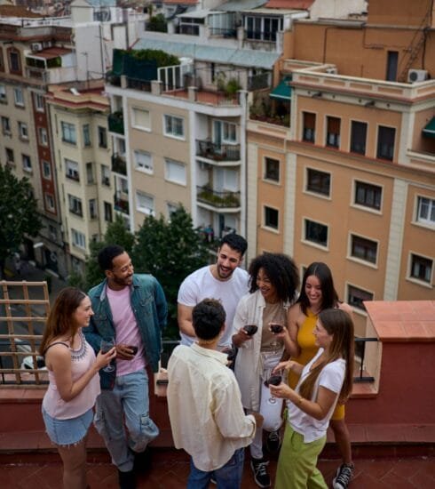 Eine Freundesgruppe steht auf dem Balkon und unterhält sich. Im Hintergrund ist der Ausblick auf eine Stadt sichtbar. Foto: CarlosBarquero/www.elements.envato.com