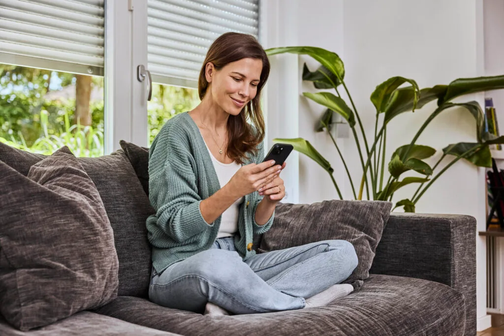 Eine Frau bedient ihr Smartphone mit der App zur Steuerung ihres intelligenten eQ-3-Produkt.