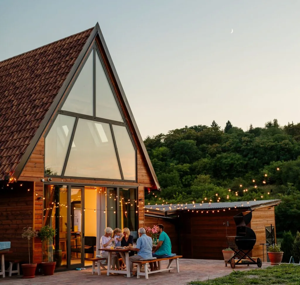 Glückliche Familie sitzt auf der Terrasse vor ihrem Haus, das mit einer Fassade in Pfosten-Riegel-Konstruktion gestaltet ist. Foto: bernardbodo/www.elements.envato.com