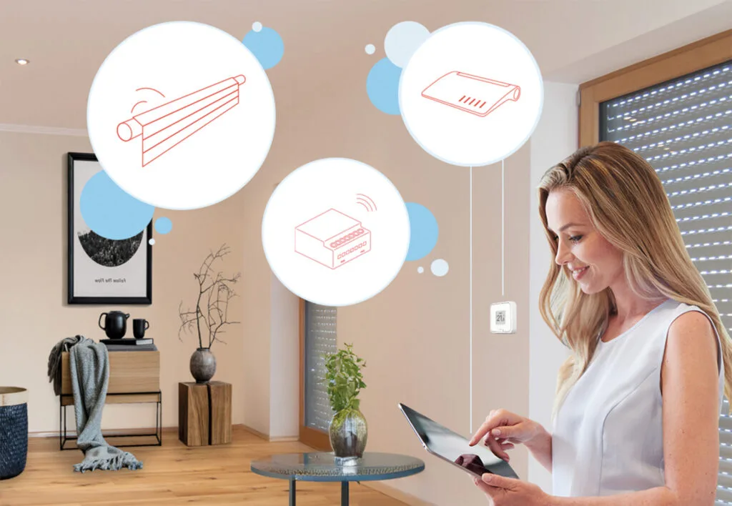 Frau mit Tablet in der Hand steht in einem hellen Wohnzimmer vor heruntergelassenen Jalousien. Smarthome Symbole sind eingeblendet.