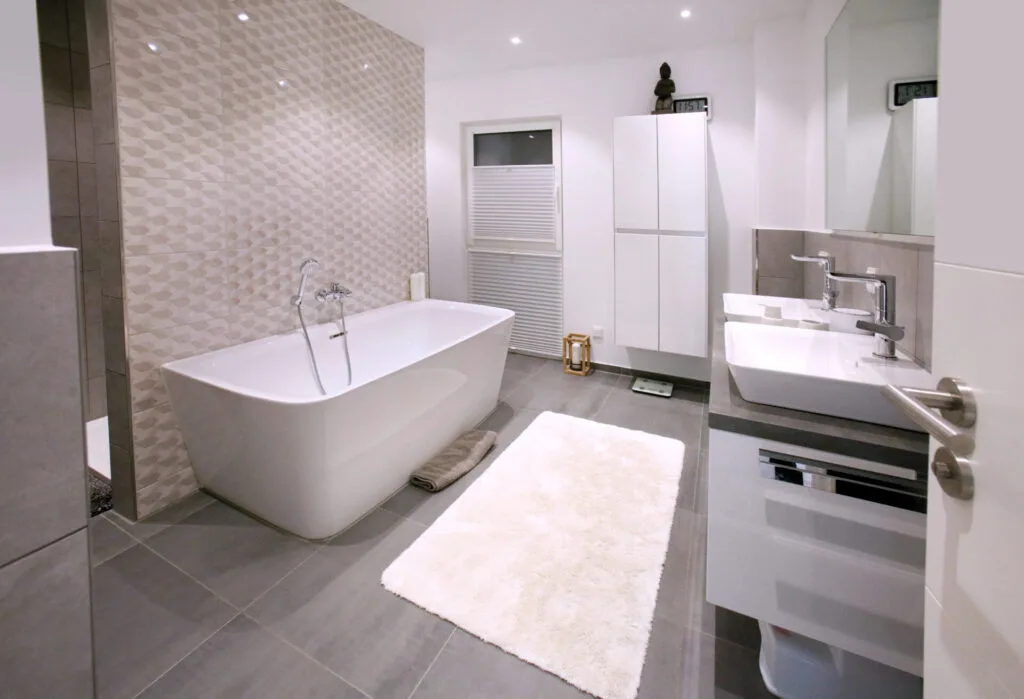 Modernes Familienbad mit freistehender, weißer Badewanne vor beigefarbenen Akzentfliesen, doppelten Aufsatzwaschbecken und grauen Bodenfliesen.