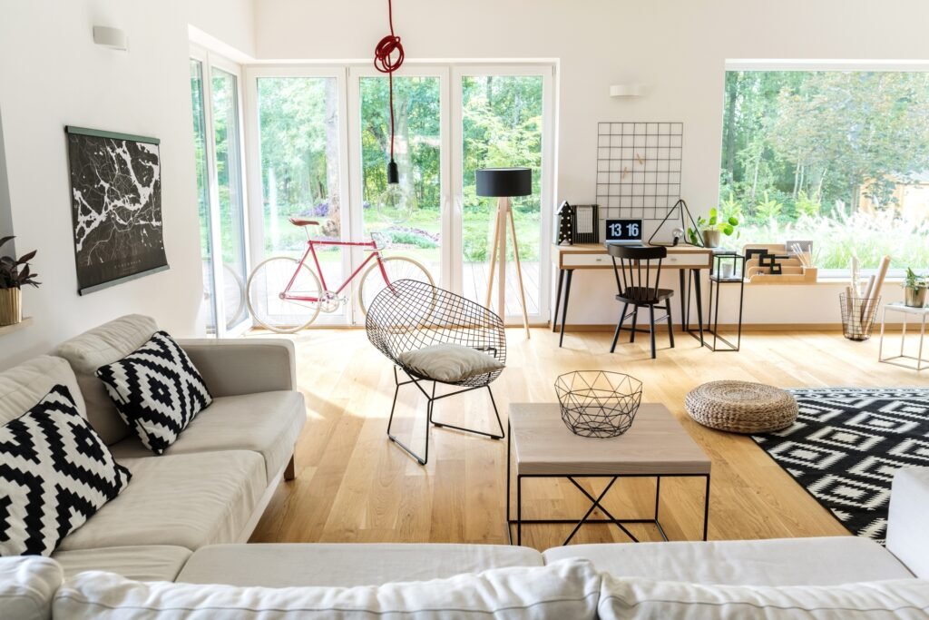 Wohnraum mit Sofaecke und Sessel, großen, teils bodentiefen Verglasungen, mit kleinem Arbeitsplatz und ein Fahrrad ist abgestellt