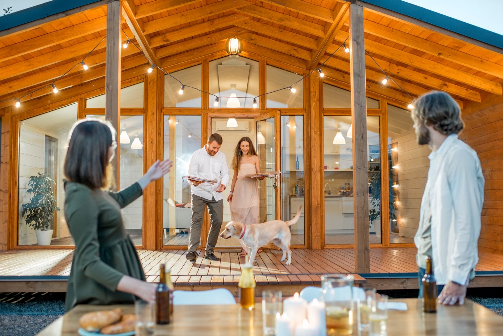 Zwei Paare und ein Hund vor einem Holzhaus in Skelettbauweise mit großzügiger Verglasung. Foto: RossHelen/www.stock.adobe.com