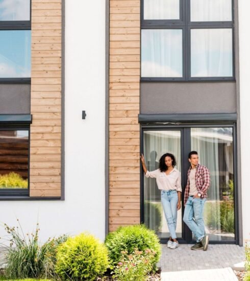 Ein Paar steht zur Kamera gewandt vor der schönen Fassade ihres Hauses.