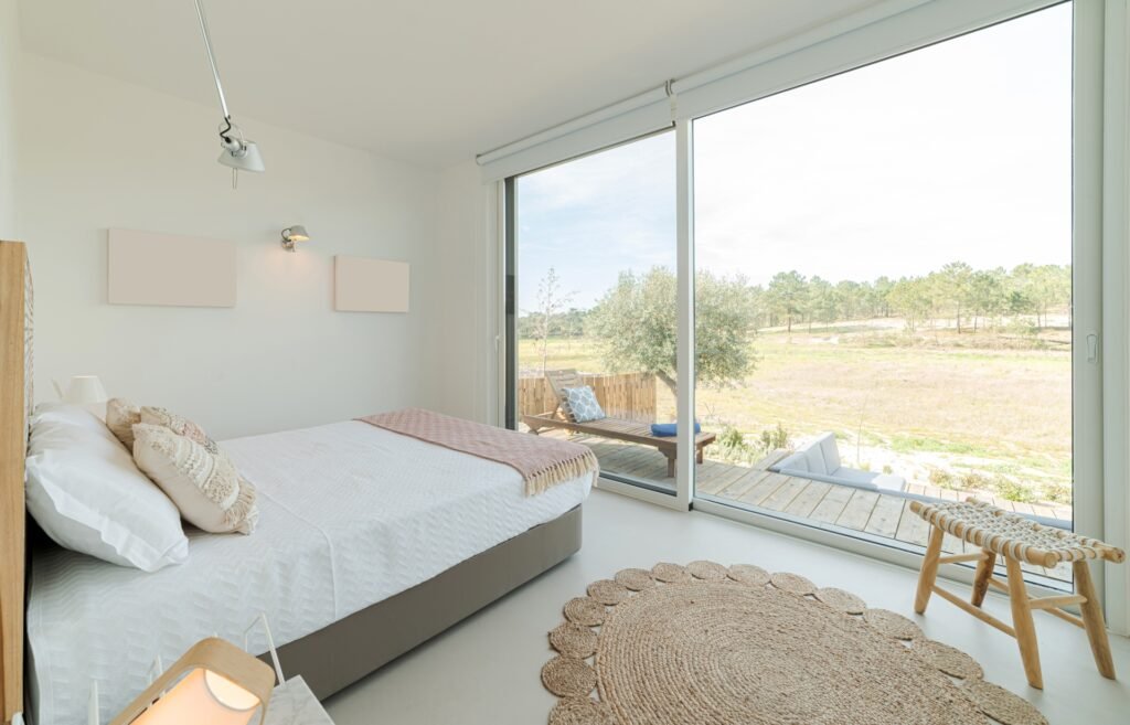 Schlafzimmer mit großer, raumhoher Glasschiebetür und Zugang auf die davor liegende Terrasse sowie Blick in die Umgebung