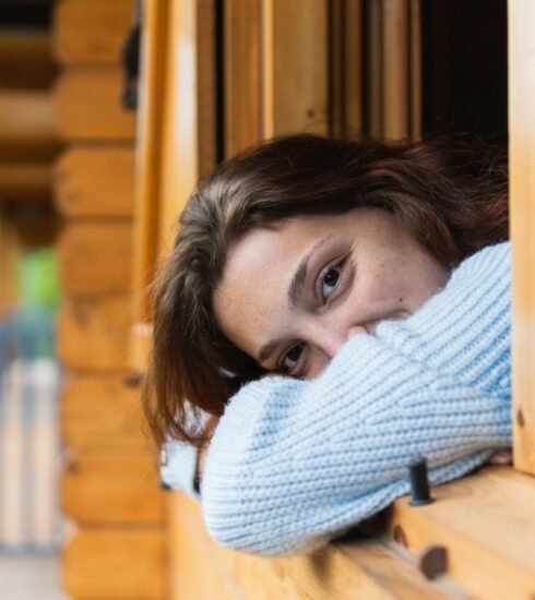 Eine Frau schaut aus dem Fenster ihres Holzhauses.