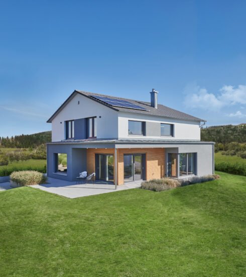 Außenansicht Musterhaus Relax von Fertighaus Weiss. Tageslicht, Blick auf das Haus und den Terrassenbereich, von Rasen umgeben.