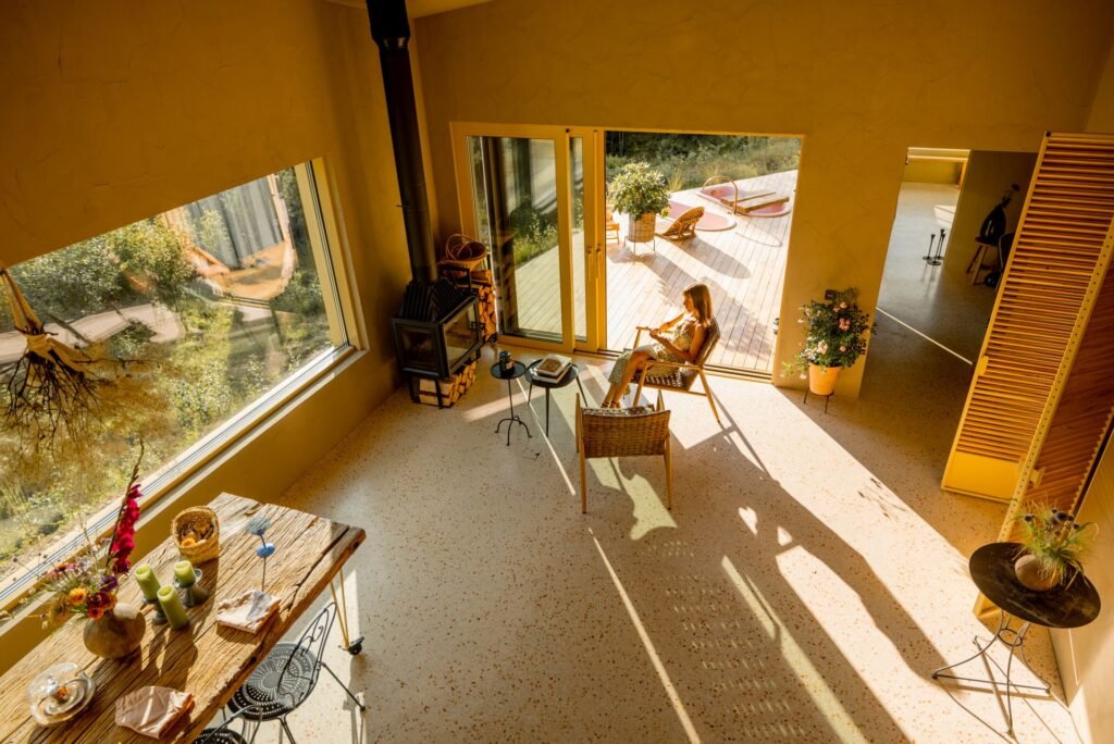 Licht fällt durch große Fenster in einen Wohnbereich. Eine Frau sitz auf einem Stuhl und wirft einen langen Schatten. RossHelen/www.elements.envato.com