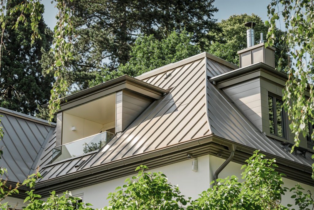 Nahaufnahme eines Aluminium-verkleideten Daches in braun umgeben von grünen großen Bäumen