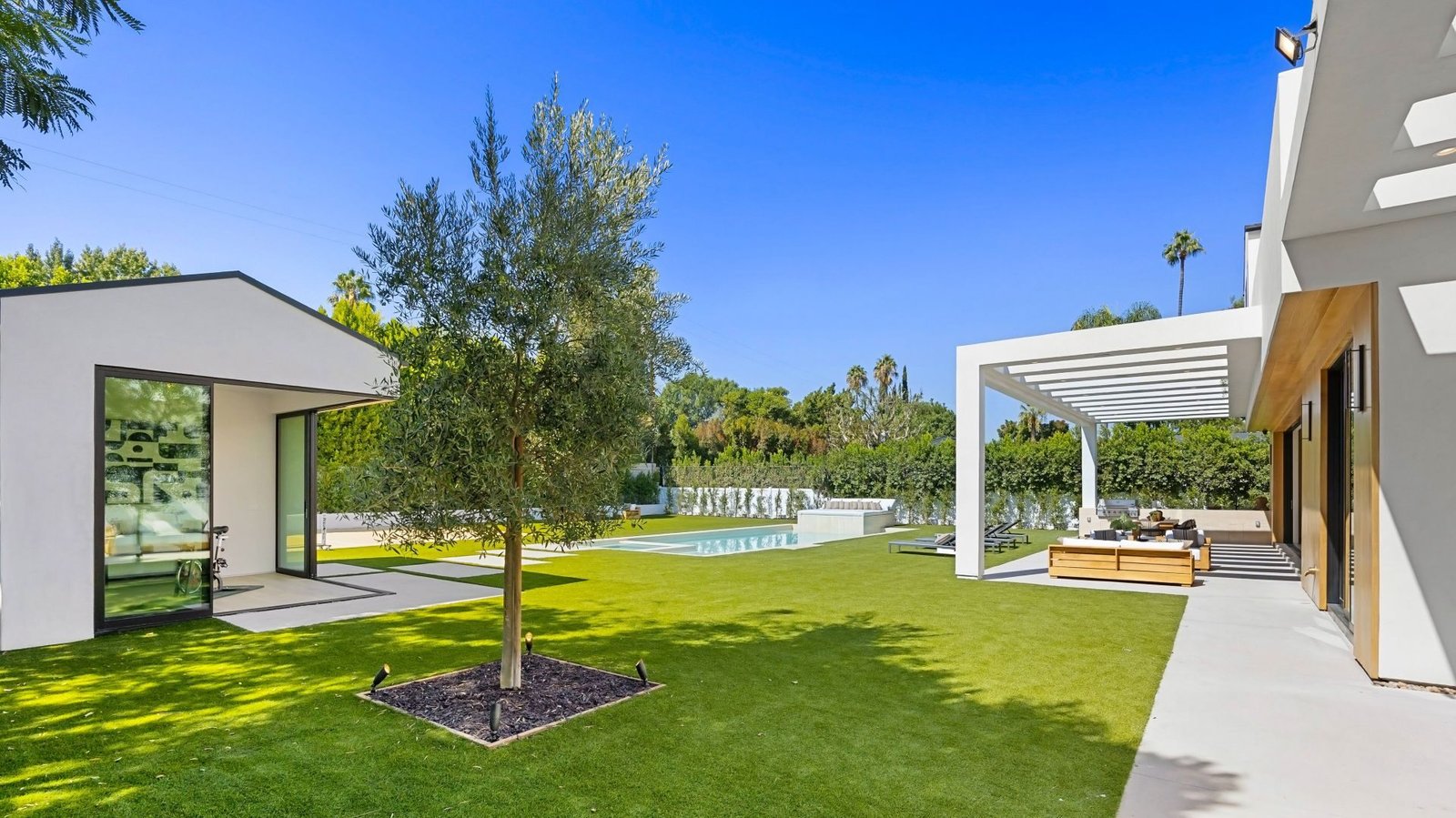 Modernes Anwesen mit Haupthaus und Nebengebäude, dazwischen Rasenfläche, junge Bäume und ein Pool.