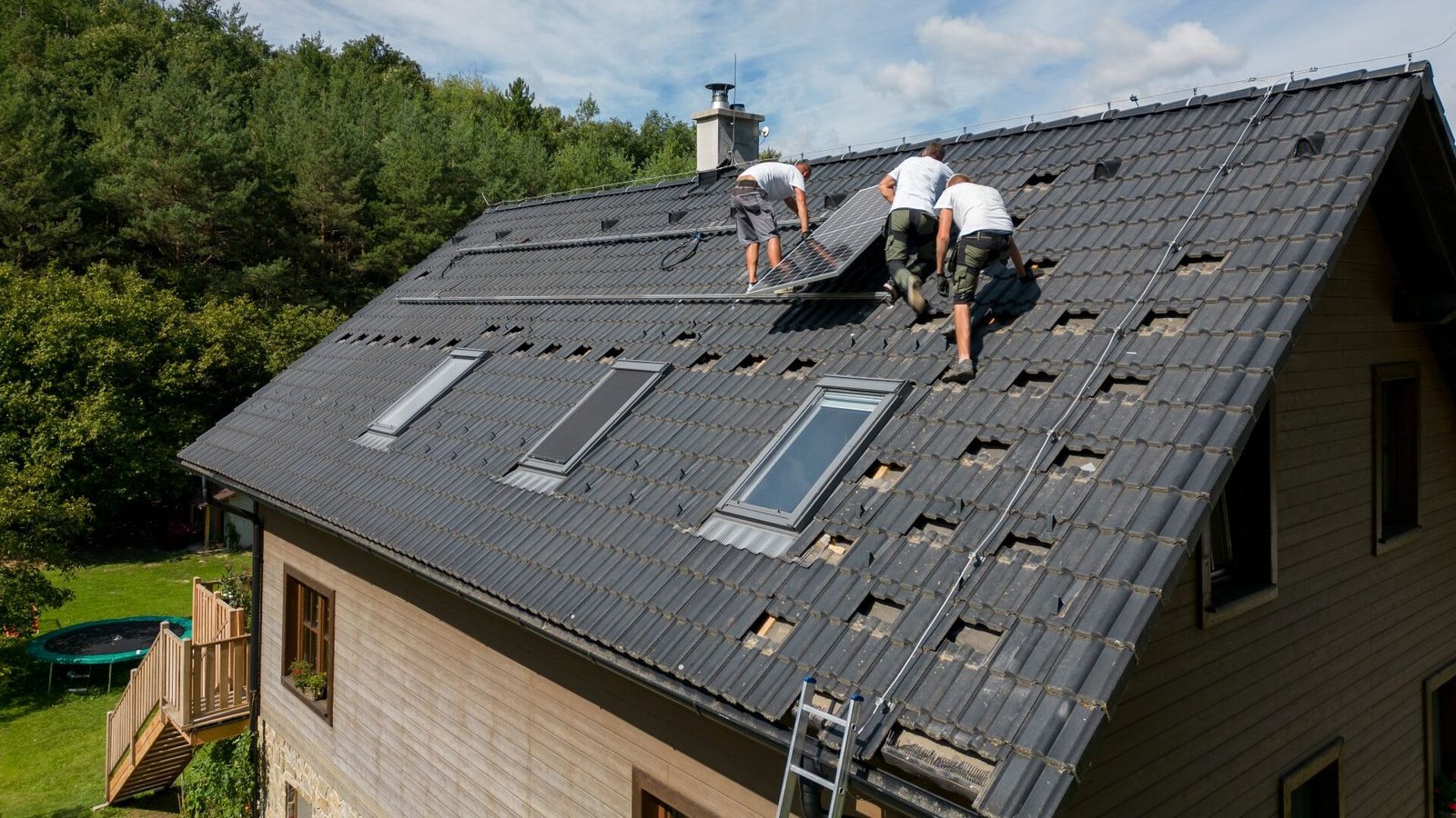 Mehrere Arbeiter intallieren eine PV-Anlage auf dem Dach eines Einfamilienhauses im Grünen.