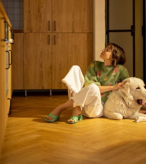 Eine Frau sitzt mit ihrem Hund auf einem schönen Fischgrätparkett.