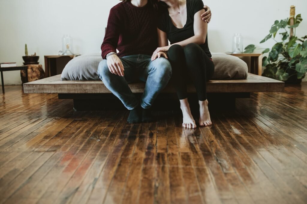 Ein Paar sitzt auf dem Bett und hat die Füße auf einem dunklen Holzboden der mit einer glänzenden Lackschicht behandelt wurde. Foto: Rawpixel/www.elements.envato.com