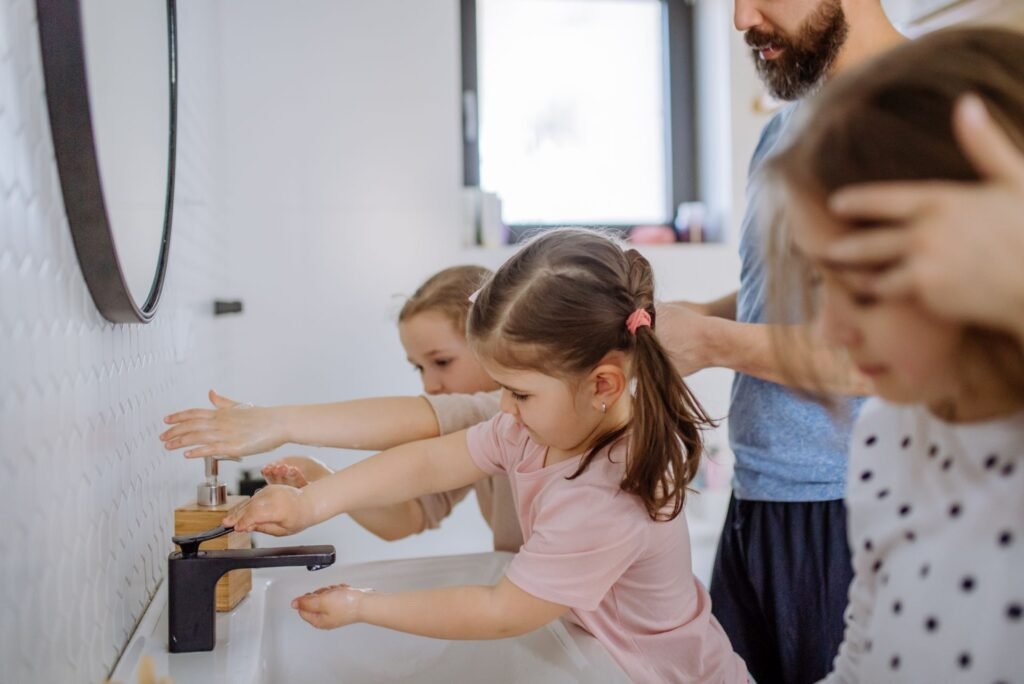 Ein Vater und drei Kinder stehen an einem Waschbecken und versuchen sich die Hände zu waschen. Foto: halfpoint/www.elements.envato.com