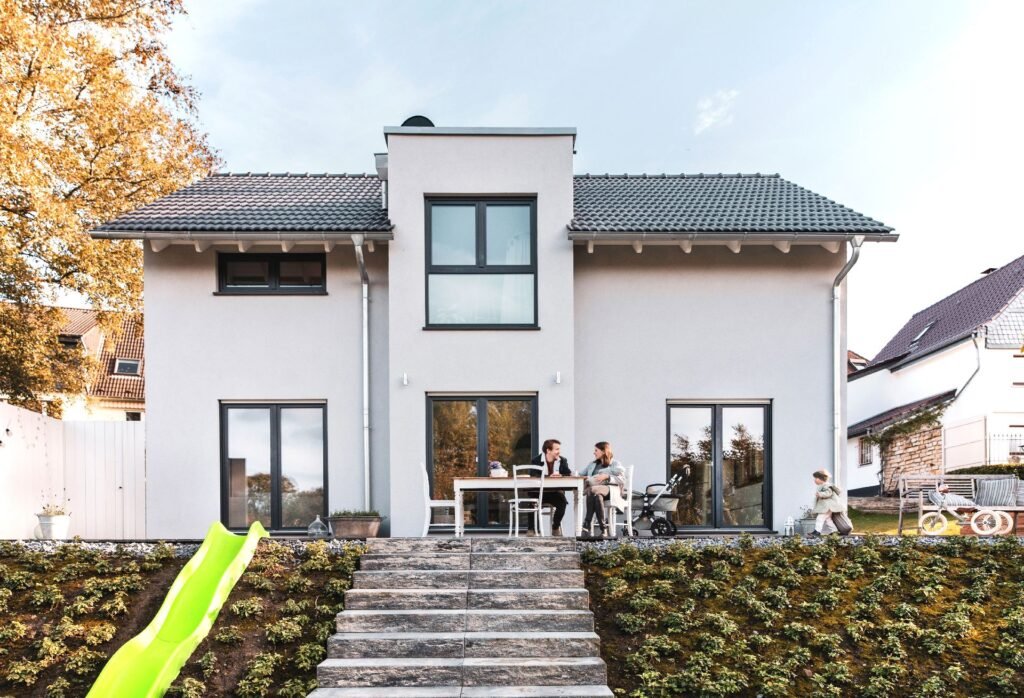 Außenaufnahme des Einfamilienhauses Vinaro von Fingerhuthaus von der Gartenseite mit der Baufamilie, die auf der Terrasse sitzt