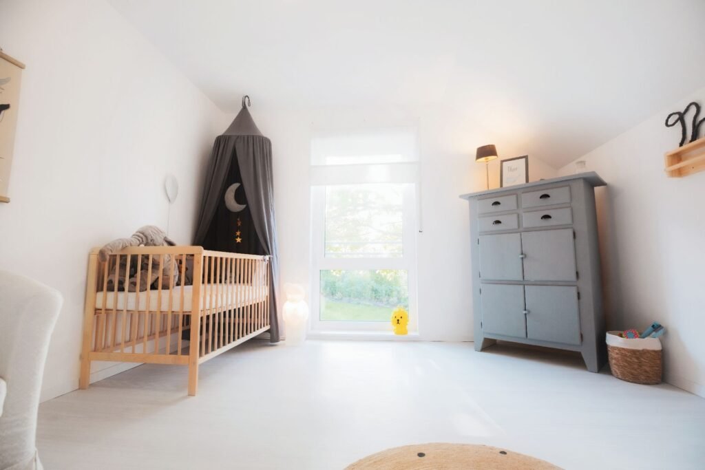 Das Babyzimmer im Haus Vinaro von Fingerhuthaus mit Bettchen mit Stoffhimmel, bodentiefem Fenster und Schrank