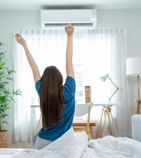 Frau in Schlafzimmer mit Klimaanlage sitzt morgens auf der Bestkante und Streckt sich