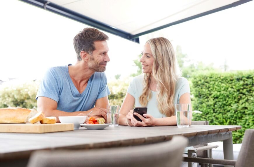 Mann und Frau sitzen auf Terrasse mit Markise und bedienen ein Smartphone