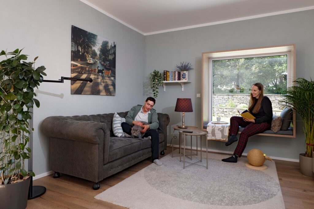 Schwörer Haus Rink Wohnzimmer Mann auf Sofa und Frau am Sitzfenster mit Katze