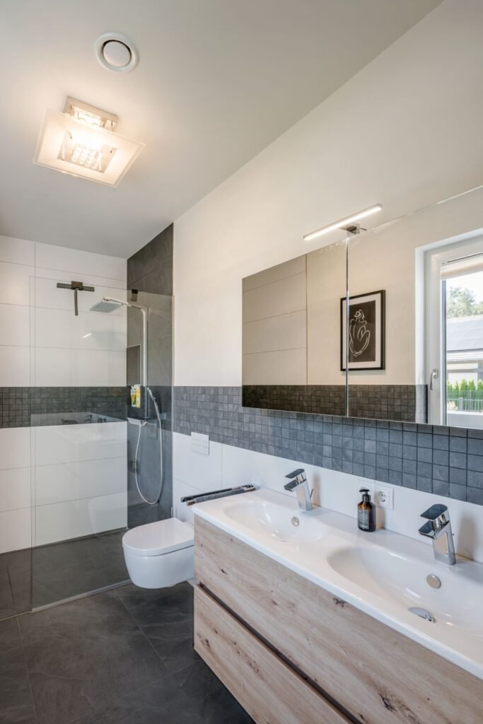 Weberhaus Graling Badezimmer mit weißen und grauen Fliesen und Waschtisch mit Holzoptik