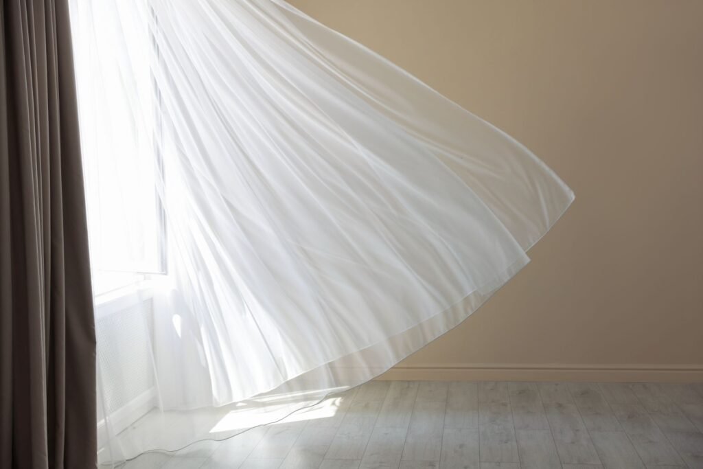 Vorhänge tanzen in dem Wind, der durch ein offenstehendes Fenster in den Raum strömt. Foto: africaimages/www.elements.envato.com