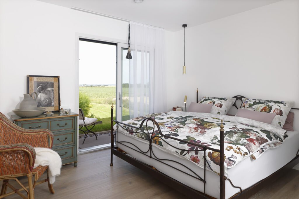 Schlafzimmer mit bodentiefem Fenster bzw. Glastür, die Blick ins Grüne und direkten Zugang auf die Terrasse bietet.