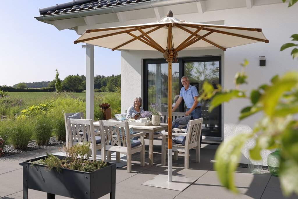 Das Bauherrenpaar auf der Terrasse ihres Bungalows, in grüner Umgebung. 
