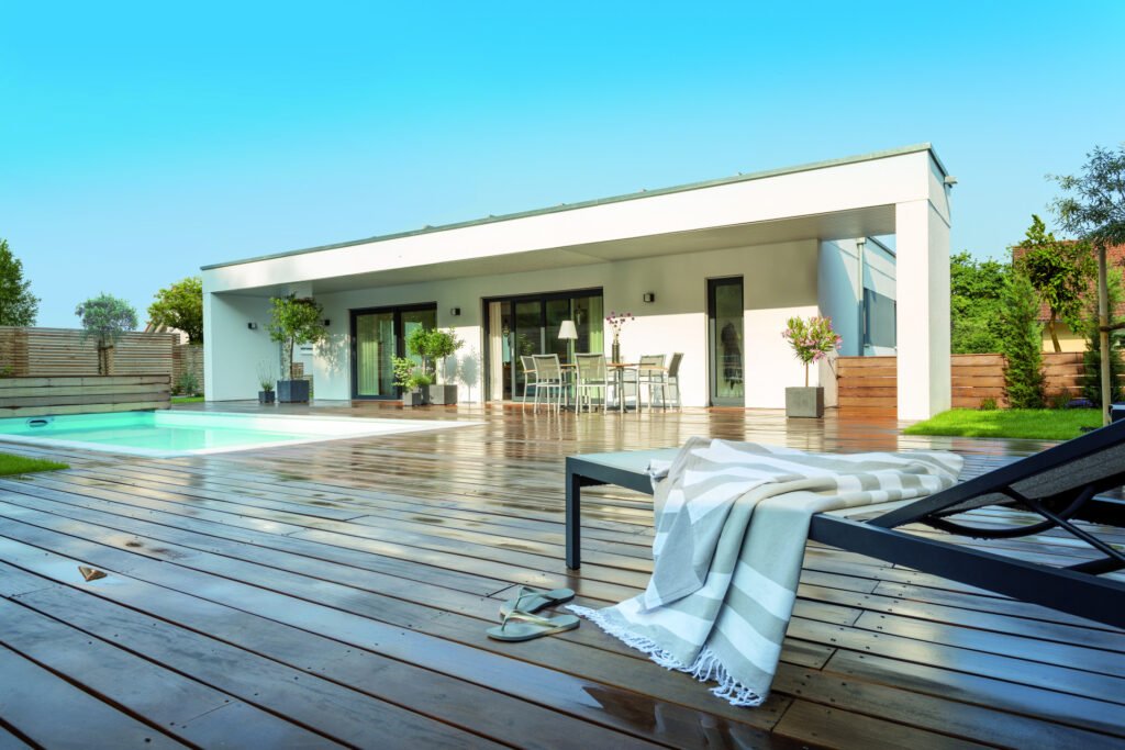 Der moderne Bungalow der Familie Nowak, mit weißer Fassade und Flachdach, davor eine große Terrasse und ein Pool.